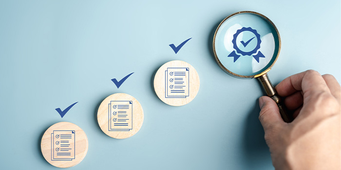 Hand with magnifying glass over quality badge beside three discs with checked checklist icons representing quality assurance