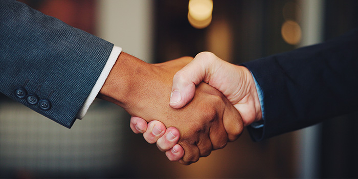 Close-up of two people in suits shaking hands in a professional business agreement, blurred office background