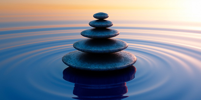 Stacked zen stones balanced on calm water with concentric ripples and warm sunset reflection, meditation and relaxation concept