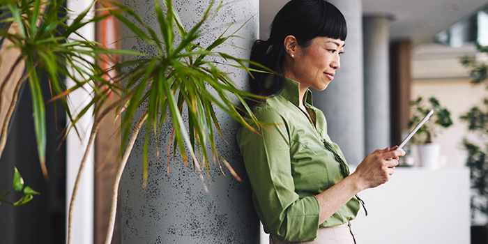 A woman using a tablet in a modern office, leaning against a column near indoor plants
