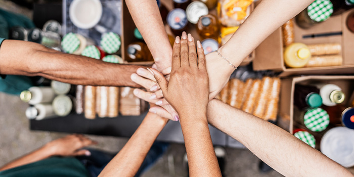 Top-down view of a group of volunteers joining hands over boxes of donated food at a community food bank, teamwork concept