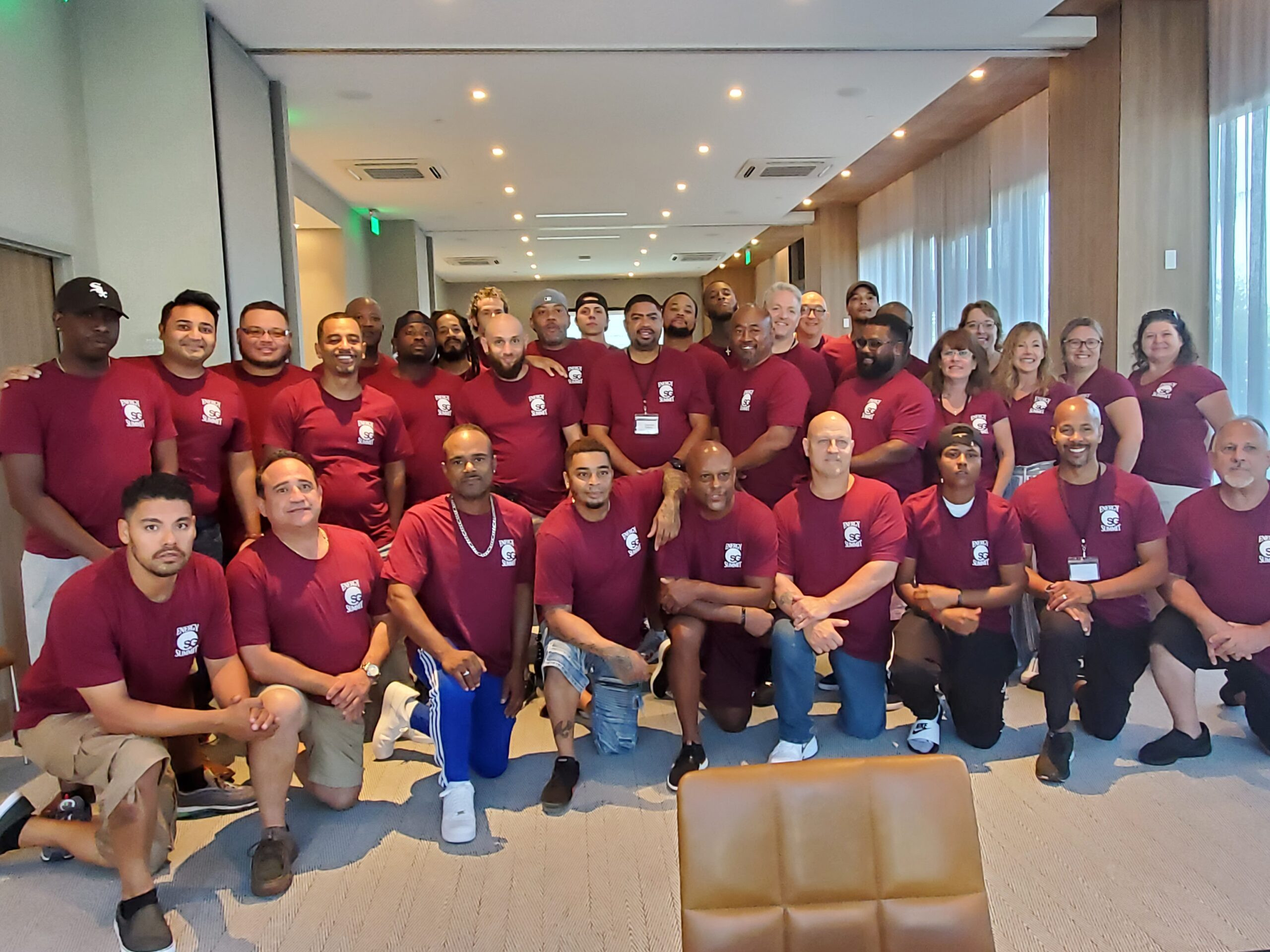 Large team group photo in maroon shirts posing indoors at a company retreat or training conference