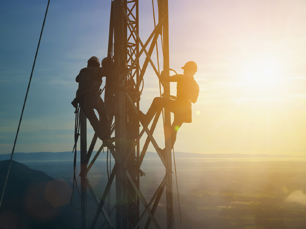 Silhouetted tower technicians performing high-altitude telecom mast maintenance at sunrise